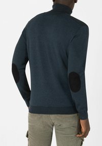 Marineblauer Strickpullover mit hohem Kragen und geripptem Saum. Mit schwarzen Ellbogenpatches und einer glatten Textur. Legere Passform, lange Ärmel.