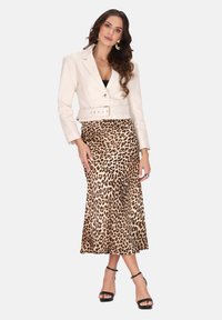 Blazer bianco corto con cintura sopra una gonna midi a stampa leopardata, che mette in evidenza una texture liscia e una vestibilità che valorizza. Tacchi neri con cinturini completano il look.