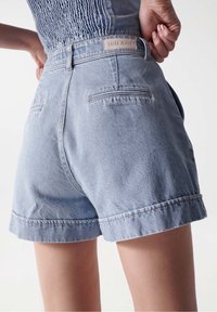 Vaaleansiniset farkkushortsit, joissa on käännetty helma, takataskut ja vyötäröllä "Salsa Jeans" -merkki. Sileä pinta, rento muotoilu.