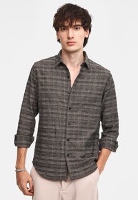 Camicia a maniche lunghe a scacchi marrone e grigia con colletto button-down, tessuto texture e bottoni neri. Maniche arrotolate e orlo curvo.