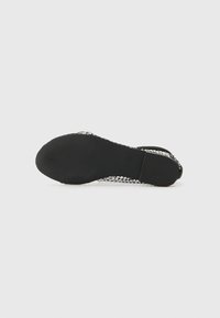 Black flat sandal with a textured sole, featuring a mesh body, open toe design, and minimal accents. Flexible material for comfort.