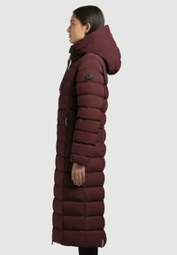 Burgunderfarbener Puffercoat mit langem, geradem Design, horizontalem Steppmuster, übergroßer Kapuze, schwarzem Reißverschluss und seitlichen Taschen.