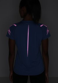 Camiseta deportiva de manga corta azul marino con detalles reflectantes rosas en los hombros y la espalda; textura suave, escote redondeado, ajuste holgado.