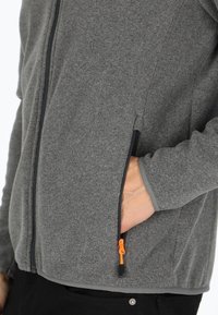 Gray fleece jacket with zippered pockets, contrasting black zippers, and an orange pull tab. Soft texture and casual design.