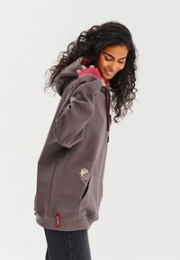 Preľahký sivý mikinový sveter s kapucňou v bordovom odtieni, rebrovanými manžetami, bočnými vreckami a béžovou nášivkou s logom na prednej strane. Mäkčený materiál z bavlneného zmesi.