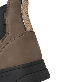 Stivaletto in suede marrone con dettagli intrecciati color tan, elastico laterale, suola nera, design curvo e cuciture visibili.