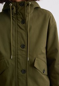 Oliwkowa kurtka z kapturem z sznurkiem, dużymi przednimi kieszeniami i czarnymi guzikami, wykonana z gładkiego, wytrzymałego materiału.