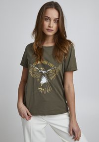 Olivengrøn t-shirt med korte ærmer, der pryder et grafisk motiv af enørn og bjerge, med teksten "AUTHENTIC LIFE" i guld- og hvide accenter.