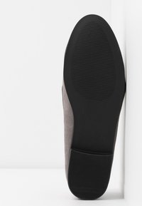 Chaussure en daim gris avec une semelle en caoutchouc noir plat, dotée de rainures texturées pour une meilleure adhérence, vue du dessous sur un fond blanc.