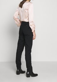 Zijden, poederroze blouse met pofmouwen en trekkoorddetail, gecombineerd met zwarte, nauwsluitende broek en zwarte enkellaarsjes.