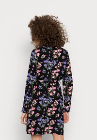 Svart klänning med långa ärmar och ett blommönster i rosa och lila, med bälte i midjan, tillverkad av mjukt material och med normal passform.