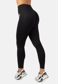 Čierne legíny s vysokým pásom, vyrobené z elastického materiálu, s hladkým povrchom a malým bielym logom na bokoch.