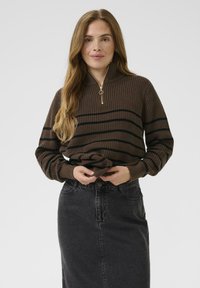 Brauner Strickpullover mit schwarzen Streifen, mit einem Halbreißverschluss-Kragen und geripptem Textur, kombiniert mit einem schwarzen Denim-Rock.