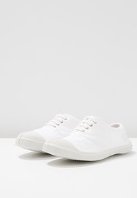 Scarpe bianche in tela con sei occhielli argentati, suole in gomma e punta testurizzata. Presentano un design a profilo basso e uno stile minimalista.