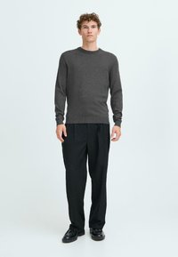 Grijze gebreide trui met lange mouwen, ronde halslijn en ribbelafwerking, gecombineerd met losse zwarte broek en zwarte schoenen. Eenvoudig ontwerp, gladde textuur.