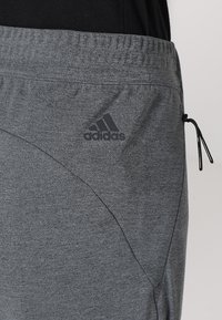 Szare dresowe spodnie sportowe wykonane z miękkiego, elastycznego materiału. Posiadają elastyczny pasek w talii, boczną kieszeń oraz czarny akcent z logo na dolnej części nogawki.