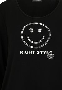 Schwarz langärmliges Shirt mit einem weißen Strass-Smiley-Gesicht und dem Text "RIGHT STYLE" darunter. Weicher Stoff mit Rundhalsausschnitt.