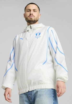 Vit vindjacka med blå accenter och dragkedja fram. Har Malmö FF-logotypen på bröstet och elastiska ärmmuddar med en justerbar huva.
