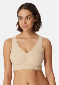 Beżowy bezprzewodowy biustonosz typu bralette z dekoltem w serek, szerokimi ramiączkami, bezszwowym krojem i gładką teksturą. Bez widocznych elementów metalowych ani zapięć.