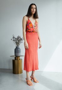 Saia de cetim coral com cintura elástica combinada com uma blusa vibrante de padrão floral. Acompanhada por sandálias laranja com tiras.