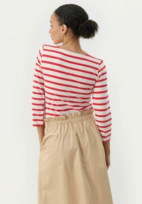 Rød og hvidstribet langærmet top med en bred udskæring, parret med en beige højtsiddende nederdel med elastisk talje.