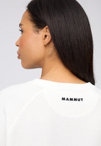 Weißer strukturierter Pullover mit rundem Halsausschnitt und Raglanärmeln. Auf der Rückseite befindet sich ein schwarzes "MAMMUT"-Logo.