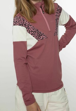 Person iført en mauve langærmet pullover med pink leopardprint og hvide farveblokdetaljer, stylet med hvide bukser.