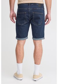 Tummansiniset farkkushortsit, joissa on käännetyt lahkeet, viisi taskua ja musta nahkainen merkki vyötäröllä. Yhdistetty beigen väristen lenkkareiden ja valkoisten sukkien kanssa.