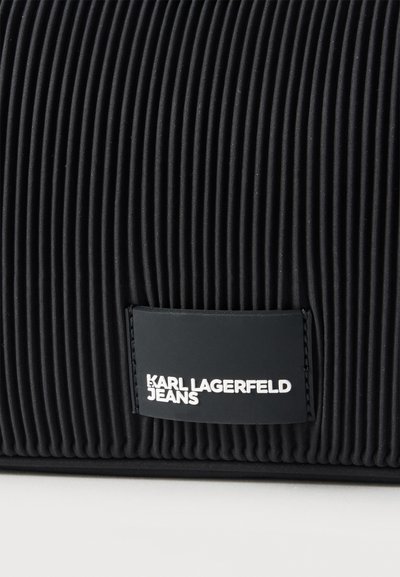 Черен плетен плат с правоъгълна черна етикета, на която е изписано „KARL LAGERFELD JEANS“ в бял текст.