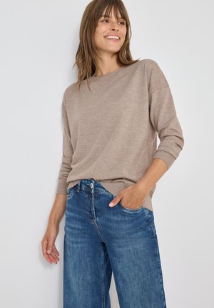 Maglione beige a maglia con maniche 3/4, abbinato a jeans a gamba larga blu scoloriti, che evidenziano un fit rilassato e una sottile trama.