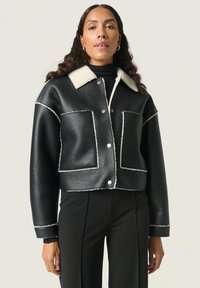 Giubbotto cropped in pelle nera con colletto in shearling, dettagli in cuciture bianche, due tasche frontali e bottoni a pressione argentati.