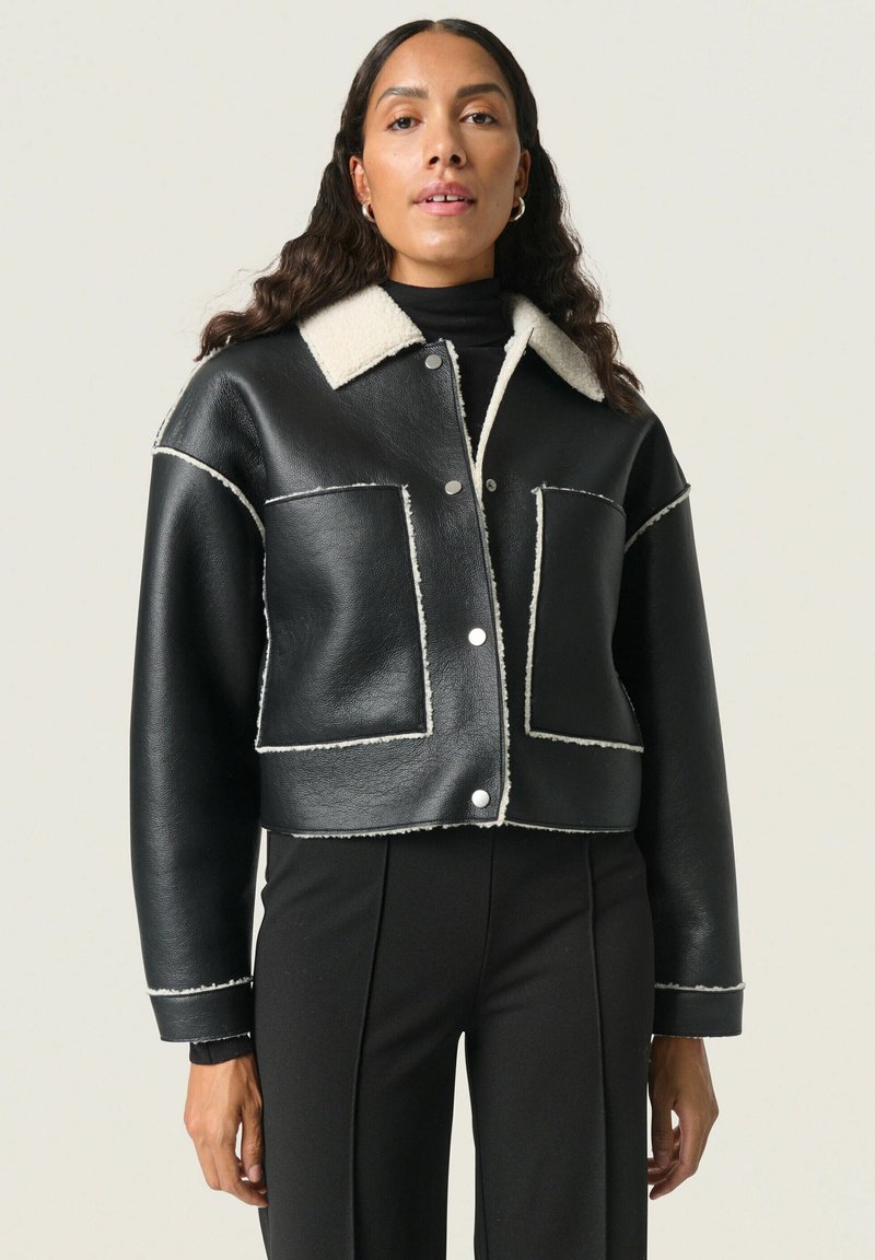 Giubbotto cropped in pelle nera con colletto in shearling, dettagli in cuciture bianche, due tasche frontali e bottoni a pressione argentati.
