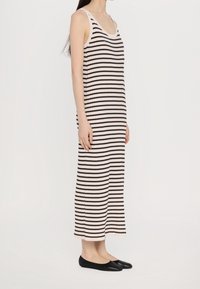 Robe maxi sans manches à rayures avec une texture côtelée, présentant des rayures horizontales alternant entre noir et crème, associée à des ballerines noires.