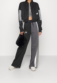 Svart kort bomberjacka med vita ränder, prickig croptop, grå och svarta träningsbyxor med sidostrepen, och en svart pälsväska.