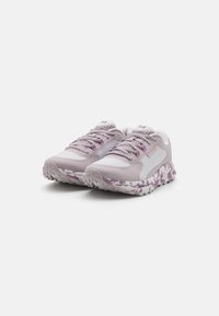 Baskets de sport violet clair avec une tige en maille texturée et un design à lacets. La semelle présente un motif camouflage dans des tons de blanc et de violet.