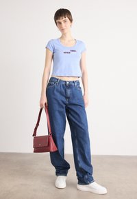 Light blue cropped t-shirt with “Calvin Klein since 1968” in dark red, paired with loose blue denim jeans and a burgundy handbag. White sneakers.