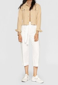 Chaqueta de mezclilla corta en beige claro con botones plateados, combinada con pantalones blancos de cintura alta que tienen un cinturón atado y dobladillos con vuelta. Zapatillas blancas.