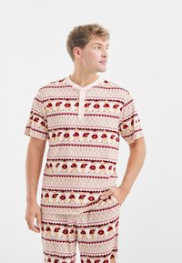 Katoenen pyjama set met een crèmekleurige basis, versierd met rode en beige geometrische patronen en berenmotieven. T-shirt met korte mouwen en knoopsluiting.