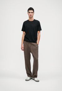 Μαύρο μπλουζάκι crew-neck συνδυασμένο με καφέ φόρμες που διαθέτουν κορδόνι. Το μοντέλο φοράει λευκά και γκρι αθλητικά παπούτσια.