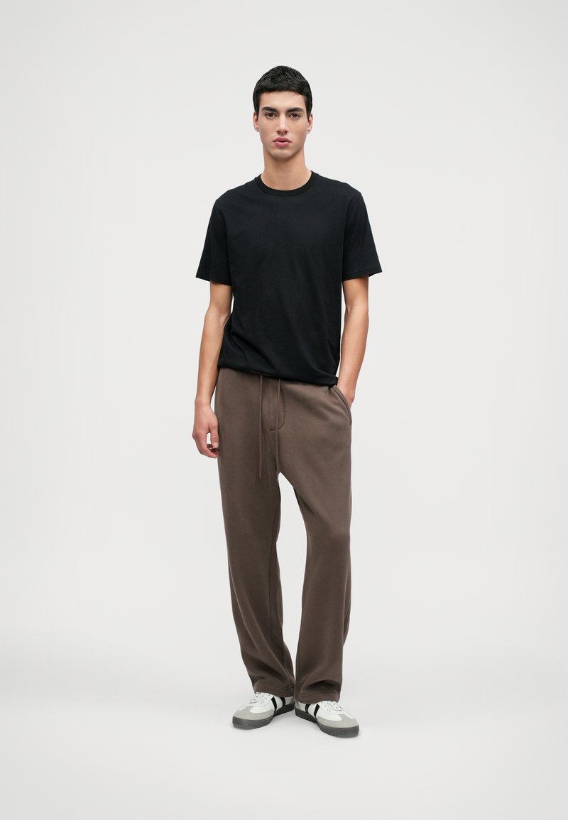 Svart t-shirt med rund hals som kombineras med bruna mjukisbyxor med dragsko. Modellen har på sig vita och grå sneakers.