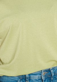 Šviesiai žalia, blizganti viršutinė dalis, pagaminta iš minkštos medžiagos, derinama su mėlynais džinsiniais šortais, turinčiais mygtuką ir kišenių detales.