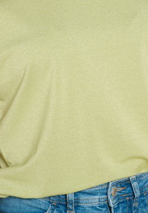 Svetlozelený, lesklý top vyrobený z mäkkej tkaniny, skombinovaný s modrými džínsovými šortkami s detailmi gombíka a vrecka.