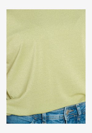 Top de un suave tejido de color verde claro y brillante, combinado con pantalones cortos de mezclilla azules que presentan detalles de botones y bolsillos.