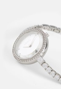 Orologio d'argento con quadrante in cristallo sfaccettato, circondato da una lunetta tempestata di diamanti, e un bracciale con pietre decorative trasparenti.
