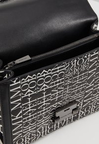 Borsa a tracolla in pelle nera con un motivo logo bianco, chiusura con zip e un accento in hardware nero lucido sulla parte anteriore.