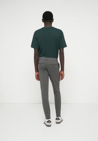 Zelené tričko s krátkým rukávem a slim-fit šedé kalhoty, oboje z měkkého materiálu, s viditelnými zadními kapsami na kalhotách. Zobrazená obuv je pohodlná.