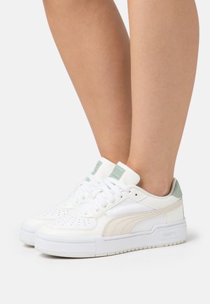 Des baskets blanches avec une tige en cuir lisse, un accent en suède vert au niveau du talon et une épaisse semelle en caoutchouc blanc. Comprend un bout perforé et un logo.