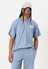 T-shirt azzurro chiaro a maniche corte, realizzato in morbido cotone, con un piccolo logo bianco sul petto a sinistra e una vestibilità comoda. Abbinato a pantaloni coordinati.