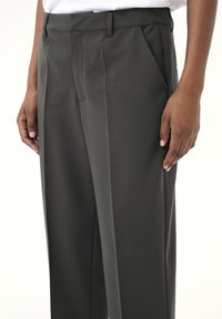 Pantalons gris à coupe décontractée avec plis sur le devant, poches latérales et texture lisse, dotés d'une taille avec passants de ceinture et d'une coupe ajustée.