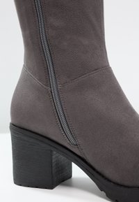 Graue Wildleder-Ankle-Boots mit einem seitlichen Reißverschluss und einem kräftigen schwarzen Absatz. Die Textur ist glatt mit einem matten Finish.